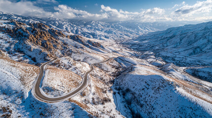 Snow-covered mountain landscape with winding road under cloudy sky in winter
