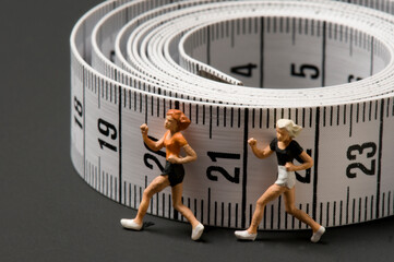 Miniature athlete figures running beside tape measure as fitness concept