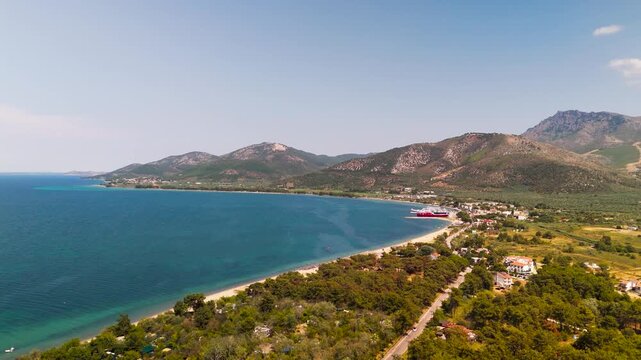 High Aerial Approach Over Green Forest to Prinos Port, Thasos, Greece, Showcasing the White Sand Beach and Turquoise Thracian Sea.