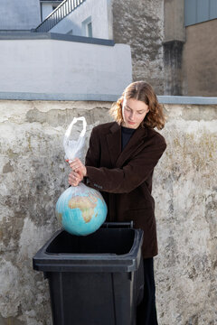 Young woman discarding globe into trash bin as environmental activism concept
