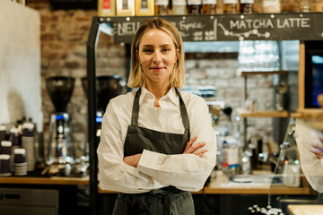 Barista in apron standing proudly in cozy cafe looking at camera