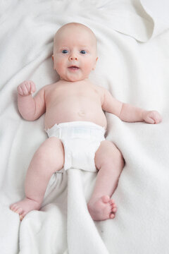 Baby lying on soft white blanket wearing diaper indoors