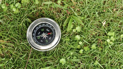 Silver magnetic compass lying on a vibrant green lawn. Concept for navigating nature, outdoor...