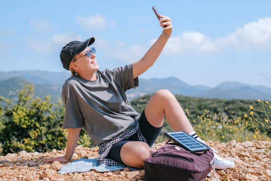 Traveler relaxing in mountains taking selfie with solar panel backpack