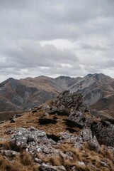 Obraz premium Rugged mountain landscape with sharp rocky peaks and dry alpine grass under a heavy overcast sky. Dramatic wilderness scenery of high altitude highlands in autumn or early spring.