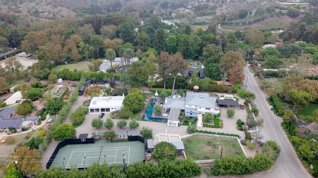 High-end homes in the Zuma neighborhood of Malibu, California with swimming pools and tennis courts on a foggy morning - aerial flyover