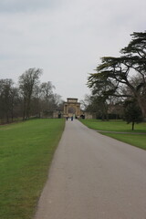 Fototapeta premium Straight Path Through a Green Park Leading to a Historic Stone Gate