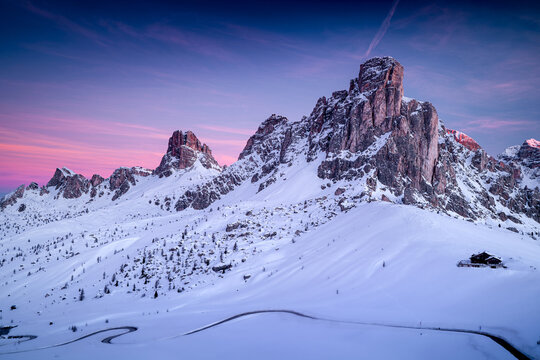 Amazing pink colors in sky before sunrise, overlooking the Dolomite peak of Ra Gusela, Giau Pass. The most beautiful mountain landscapes in Italy with winding road.