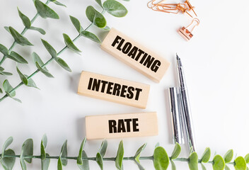 Wooden blocks with text floating interest rate on background with green leaves and office supplies, symbolizing variable loan
