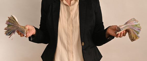 person wearing a black jacket holds stacks of banknotes in two hands, showing significant amount of money. woman holds cash in Ukrainian hryvnia.