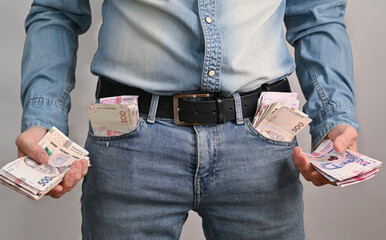 Man confidently shows his cash, pockets bulging with bills and hands full of cash. financial success and material achievement. successful man holds bundles of money in his hand. wealth, prosperity.