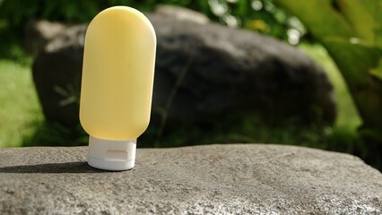 A single yellow silicone travel bottle standing upright on a grey rock with a lush green garden background. © agung