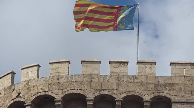 view of The flag of Valencia (Reial Senyera)  and the Torres de Quart (Quart Towers), one of the two remaining gates of the old city wall of Valencia, Spain.
