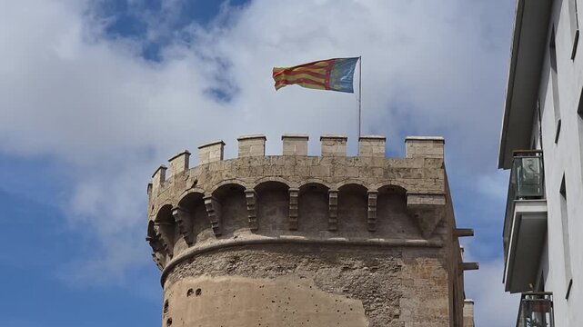 view of The flag of Valencia (Reial Senyera)  and the Torres de Quart (Quart Towers), one of the two remaining gates of the old city wall of Valencia, Spain.