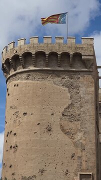 view of The flag of Valencia (Reial Senyera)  and the Torres de Quart (Quart Towers), one of the two remaining gates of the old city wall of Valencia, Spain.