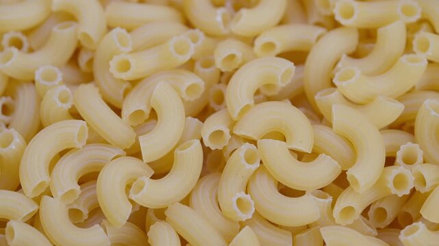 Bulk uncooked macaroni heap suggests wholesale stock factory packaging, dense pile conveys volume and commerce, neutral tones suitable for food industry or supply chain visuals