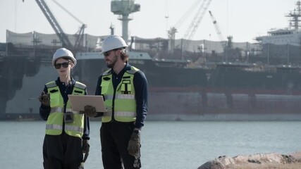 Workers at port discuss project details near large ships in the background