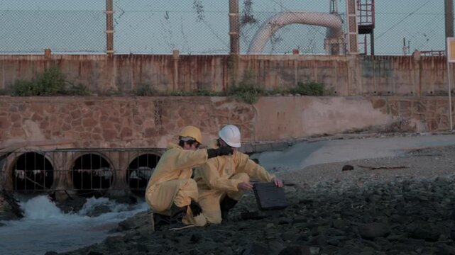 Technicians collect samples along the riverbank at sunset near an industrial area