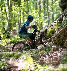 Naklejka premium Man mountain biker navigating a forest trail with helmet and gear on a sunny day