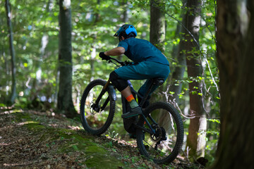 Rider on a forest trail: mountain biking in lush woods with helmet and gear