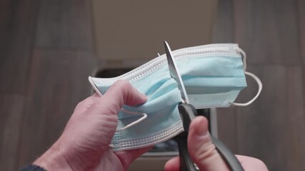 Man cutting a medical mask with scissors and throwing it into the trash bin. Concept of the end of the COVID-19 pandemic and returning to normal life.