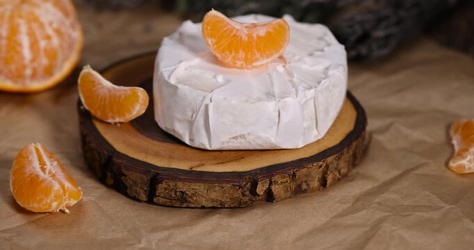 fresh white cheese with white mold lies on a wooden board on crumpled yellow paper, soft round cheese and juicy sweet orange tangerines