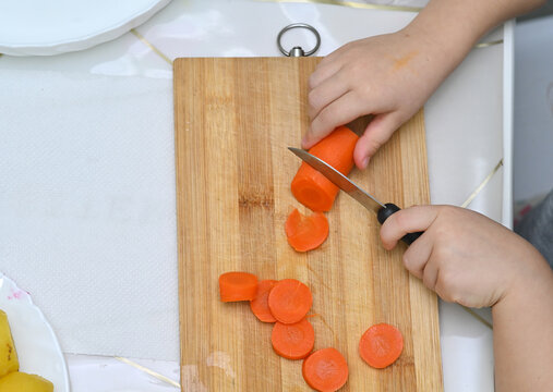 Montessori-style learning in kitchen as child gains independence with safe tasks. Educational moment showing practical life skills development. child cuts boiled carrots