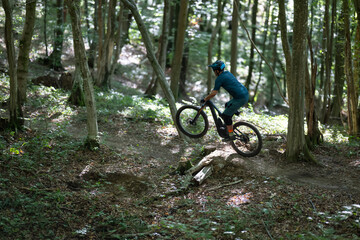 Naklejka premium Mountain biker in blue kit rides a rocky forest trail on an electric mountain bike