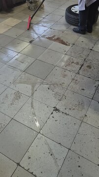 Cleaning worker garage floor maintenance: Employee uses a rubber squeegee to push water and dirt across the wet tiled floor of an auto service bay.
