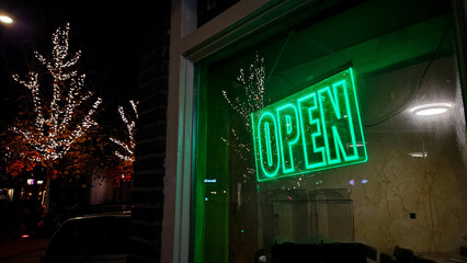 Open sign window store. Neon green open sign on restaurant window. Store entrance opening closed signage in shop. Neon sign glow next to shop entrance.