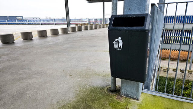 White recycle symbol logo on a green bin with black trash bag and a bamboo nature background.