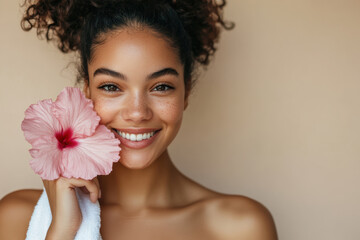 Young woman smiling with pink hibiscus flower on a plain background