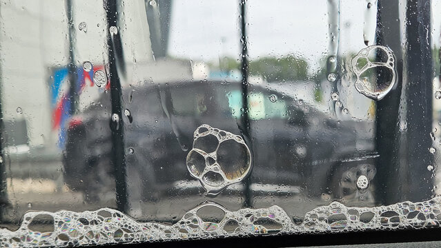 Soap foam and bubbles on a car window inside a car wash, vehicle cleaning process.