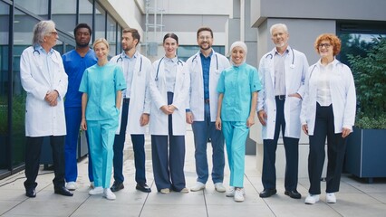 Medical team standing outside clinic smiling and looking directly at camera. Group posing together showing unity and confidence. Professionals presenting friendly attitude during calm moment.