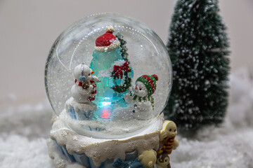 Snow globe with fir tree and cute snowman on blurred background.