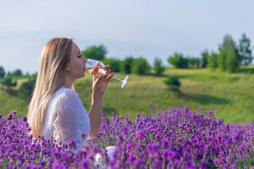 Woman in white dress at picnic in lavender field holding a glass of wine
