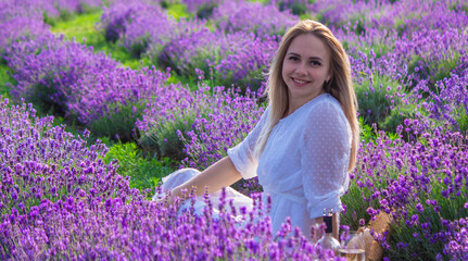 Woman in white dress at picnic in lavender field holding a glass of wine