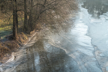 Aufsicht teilweise gefrorener Fluss Neckar bei Neckartenzlingen mit kahlen B&auml;umen an der vereisten Uferb&ouml;schung