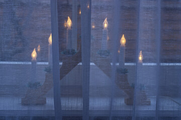 Electric Christmas candle holder covered by a curtain inside a room.