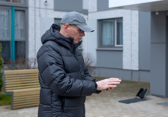 A mature man uses a smartphone outdoors to search for a location and plan a route in a residential