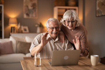 Warm Moment: Grandparents Laughing And Waving At Laptop In Cozy Living Room At Home