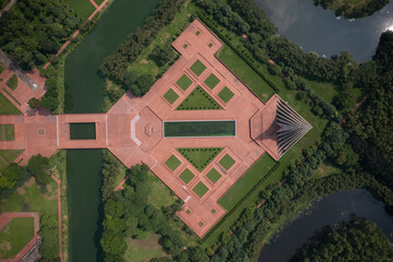 Aerial view of a monument with symmetrical brick patterns juxtaposed against the lush green vegetation and dark waterways, Savar, Dhaka Division, Bangladesh.