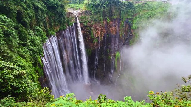 The multi-tiered Tumpak Sewu waterfall, with its lush greenery and wide stream of water flowing into a deep, semi-circular basin on the island of Java. Near Mount Semeru. Indonesia. 4К