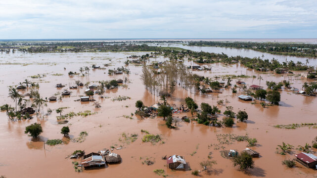 Aerial view of floodwaters engulfing homes and trees, creating a landscape of muted browns and greens under a cloudy sky, Buzi, Sofala Province, Mozambique.