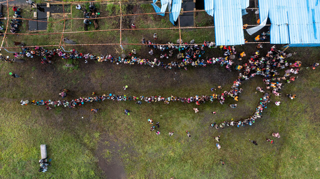 Aerial view of people lined up in an outdoor area, creating a stark contrast against the muted green landscape, Dondo, Sofala Province, Mozambique.