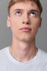 Fototapeta premium Young man gazing upward with a thoughtful expression, white tee, studio lighting, neutral backdrop, quiet moment of curiosity and reflection, modern casual mood in a controlled studio setup
