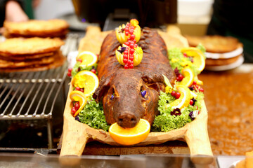 Grilled suckling piglet in spit roast. Traditional whole pig roasted on barbecue spit. Popular delicious and crispy roasted piggy on christmas fair