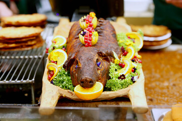 Grilled suckling piglet in spit roast. Traditional whole pig roasted on barbecue spit. Popular delicious and crispy roasted piggy on christmas fair