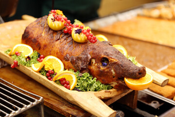 Grilled suckling piglet in spit roast. Traditional whole pig roasted on barbecue spit. Popular delicious and crispy roasted piggy on christmas fair
