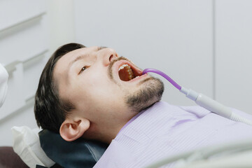 Young Caucasian male patient with irrigator tip in oral cavity in dental office.